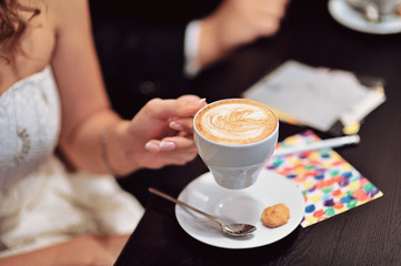 A newlywed couple drinking hot coffee or tea with sweet dessert in warm cozy cafe with wedding bouquet on the table. Atmoshere of happiness of new family and love tenderness
