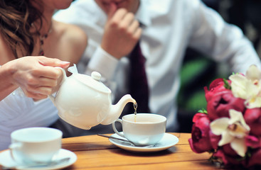 A newlywed couple drinking hot coffee or tea with sweet dessert in warm cozy cafe with wedding bouquet on the table. Atmoshere of happiness of new family and love tenderness