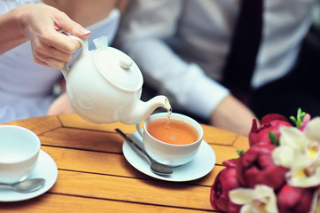 A newlywed couple drinking hot coffee or tea with sweet dessert in warm cozy cafe with wedding bouquet on the table. Atmoshere of happiness of new family and love tenderness