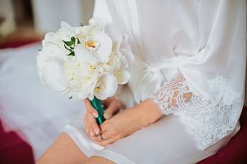 Obraz na płótnie Canvas White wedding bridal bouquet with emerald green tape in the hands of bride before wedding ceremony with decoration a lot of flowers and colorful tapes shot taken by selective soft focus and macro