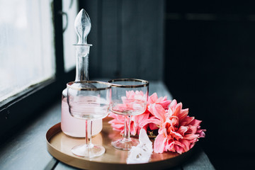 close-up of a tray with glasses of decanter and a large pink flower that stands on a wooden background near the window