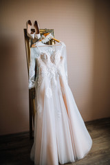 wedding lacy white dress, lace garter, shoes hanging on a gold mirror against a background of beige wall