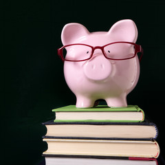 Piggy bank or piggybank wearing glasses standing on a stack of school book in front of a classroom blackboard college fees saving fund photo square format