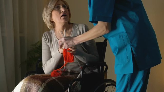 Nurse taking away needles from woman with Parkinsons disease trying to knit