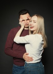 Portrait of a beautiful young couple in love posing at studio over dark background. The girl plays with the face of her boyfriend
