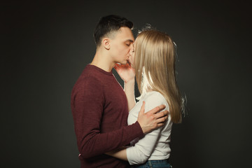 Portrait of a beautiful young couple in love posing at studio over dark background. Guy and girl kissing close up