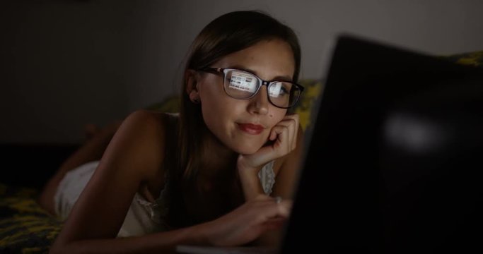 4k, Attractive young woman working on her laptop whilst lying down on a couch late at night.