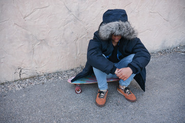 Boy sitting on skateboard wearing winter jacket hiding his face