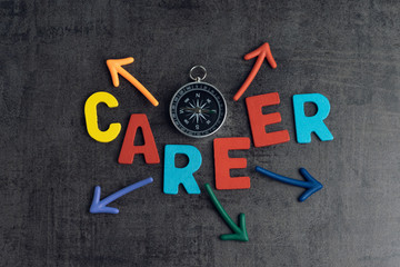 Company career path opportunities concept by colorful wooden alphabets as word CAREER and compass with magnet arrows pointing multi directions on dark black chalkboard cement wall