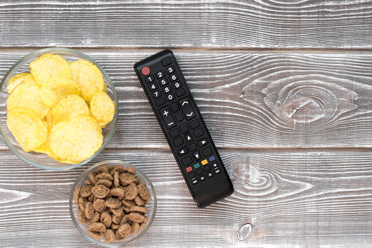 chips, crackers, a remote from the TV on a wooden background. football fan. home rest.