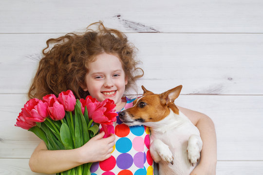 Laughing girl hugging a puppy and holding red tulips.