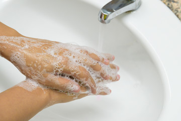 Woman washing hands with soap under the faucet with water  in the bathroom.