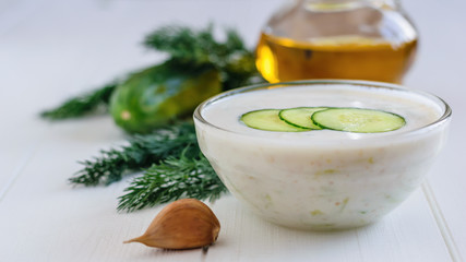 Freshly made tzatziki in a glass bowl with garlic and parsley on a white wooden table.