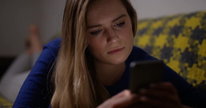 4K Girl checking her smartphone at night, her face illuminated by light from the screen