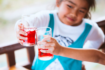 Two asian child girl clinking glasses of fresh red juice water with ice and drinking together after finish their homework in the summer time