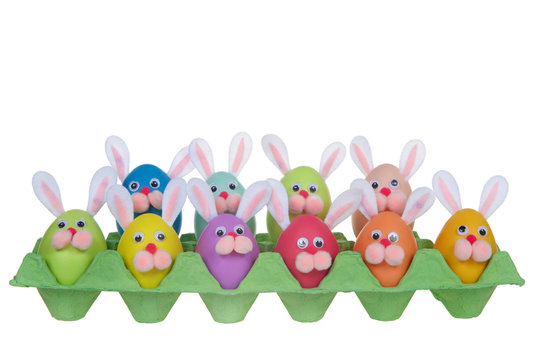 Colorful decorated Easter Eggs with bunny faces and ears sitting in an egg carton isolated on white backgound. Fun easter concept.
