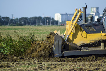 The yellow tractor with attached grederom makes ground leveling.