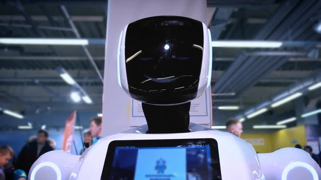 Portrait of a new modern white robot. The robot turns its head, looks into the camera. Exhibition of robots and high robotic technologies.