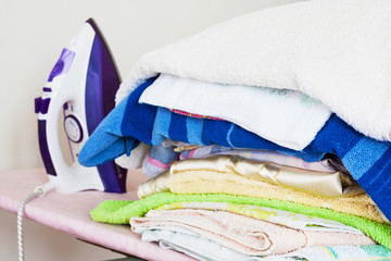 Pile of of washed clothes from the laundry with electric iron. Closeup, selective focus.