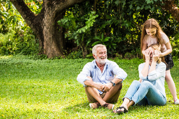 Fototapeta premium Happy family having fun together in the garden. Father, mother and daughter sitting on grass in a park.