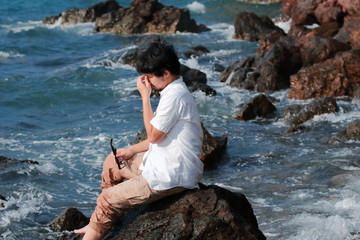 Frustrated upset young Asian man taking off glasses and close his eyes at sea coast.