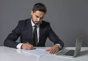 Young concentrated bearded man sitting at the table and reading agreement. Copy space in right side