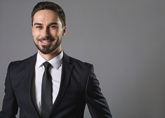 Sense of joy. Waist up portrait of bearded joyful man in business suit, he is looking at camera with felicity. Isolated on grey background and copy space in right side