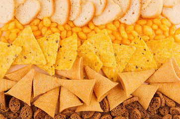 Bright spicy snacks collection -  nachos, ruddy toasts, rye croutons, corn sticks as chess background. Top view, closeup.