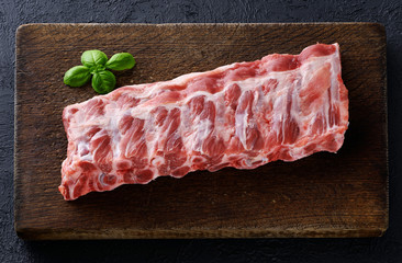 Raw fresh pork ribs and basil on a dark wooden background.