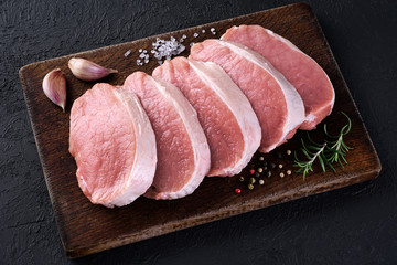 Raw sliced pork loin with salt, pepper, rosemary and garlic on a dark background. Fresh meat. - obrazy, fototapety, plakaty