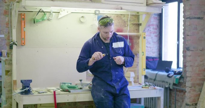 A man in a carpentry shop is standing at a bench and sharpening a pencil