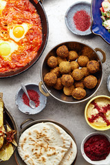 Overhead image of traditional jewish and middle eastern food: falafel, shakshuka, hummus, roasted eggplants and spicy beetroot dip. Israeli cuisine concept