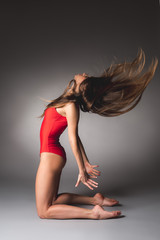Side view of slim girl in red leotard making choreographic movement while standing on knees