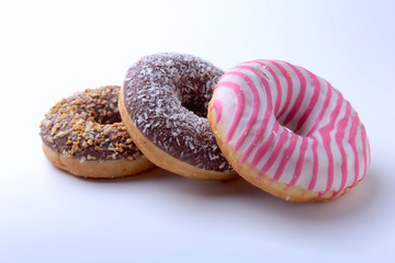 Fototapeta na wymiar Assorted doughnuts in the glaze, colorful sprinkles and nuts on a white background.