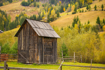 Obraz premium Autumn scenery landscape with colorful forest, wood fence and hay barns in Prisaca Dornei, Suceava County, Bucovina, Romania