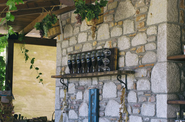 Wine bottles and glasses on a shelf fixed on a stone wall decorated with baskets of grapes