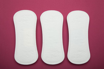 Three menstrual pads on a red background, close-up.