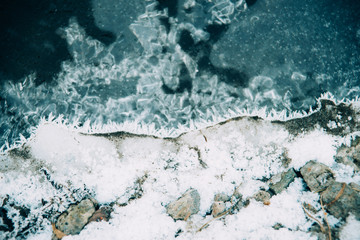 Ice fragments under thin layer of frozen river water. Dark blue natural background