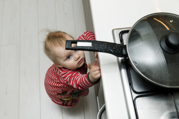 child safety at home concept - toddler reaching for pan on the stove in kitchen