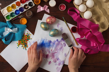 Happy easter. Painting Easter eggs on a background of a dark wooden table. Are visible Female hands