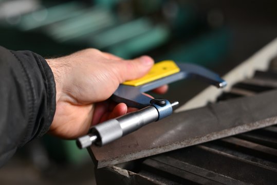 Elderly worker looks in the drawing to see detail sizes. The man turner measures the dimensions of the part on a micrometer, and also uses a sliding caliper.