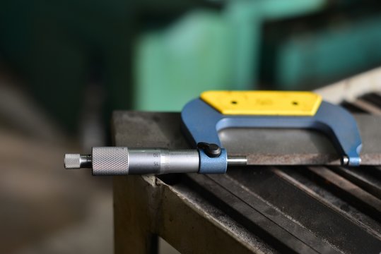 Elderly worker looks in the drawing to see detail sizes. The man turner measures the dimensions of the part on a micrometer, and also uses a sliding caliper.