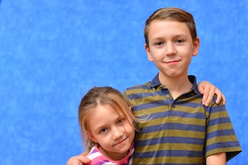Cute couple of kids in casual clothes are giving high five, looking at camera and smiling, on gray background