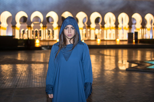 Night shot of beautiful young woman wearing traditional Arab clothes at Mosque Abu Dhabi, United Arab Emirates.