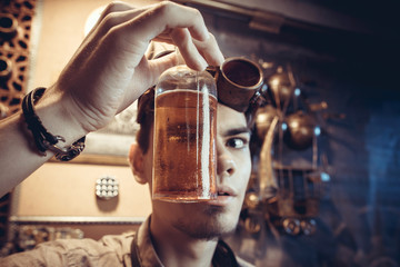 Portrait of a young mad scientist dressed in steampunk style and glasses in his fantastic laboratory with antique bottles.