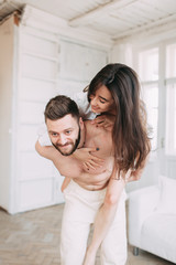 Fototapeta premium Young happy couple at home, cuddling, and kissing are. Beautiful Sunny morning with your loved ones in pajamas mad and laugh.