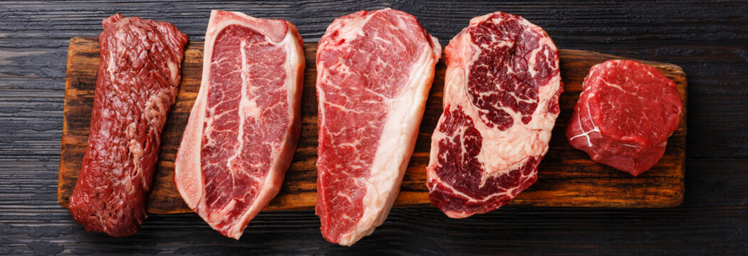 Variety of Raw Black Angus Prime meat steaks Machete, Blade on bone, Striploin, Rib eye, Tenderloin fillet mignon on wooden board