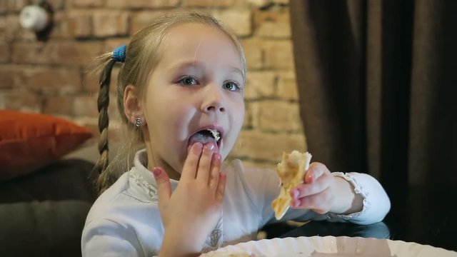 little girl in a cafe eats pizza, licks her fingers. Concept: you will lick your fingers
