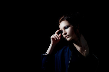 The fashion-style girl holds her hand thoughtfully at the head on a black background with a place for text in a low key