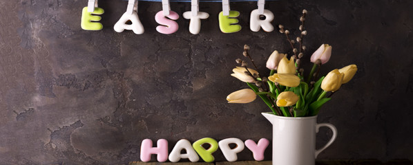 Lettering from cookies Happy Easter and bouquet tulips on stone background.